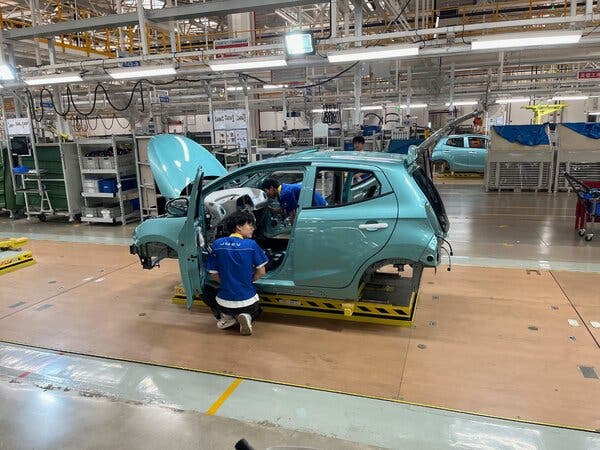 Dos personas atendían piezas de un coche en una sala de ensamblaje.